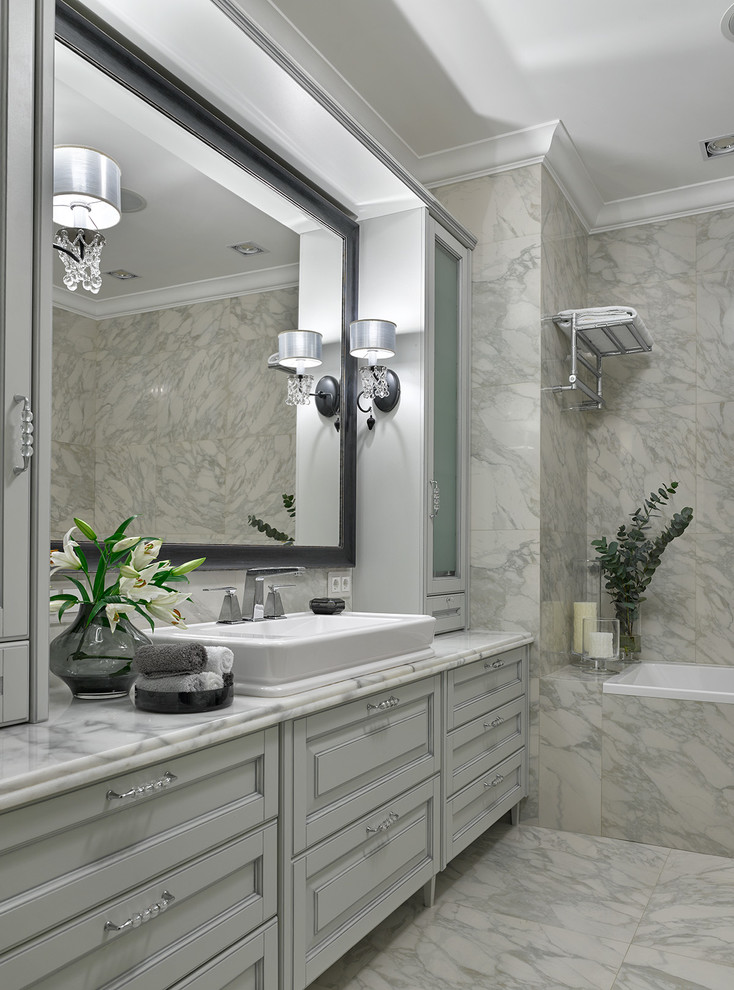 This is an example of a traditional master bathroom in Moscow with recessed-panel cabinets, white cabinets, white tile, white walls, marble floors, a vessel sink, marble benchtops and a drop-in tub.