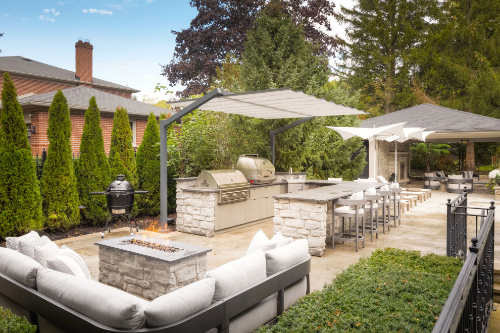 Photo of a large contemporary backyard patio in Toronto with an outdoor kitchen, concrete pavers and an awning.