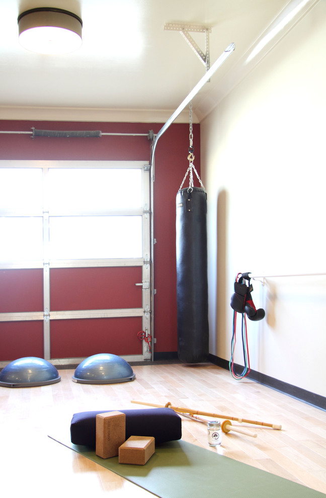 This is an example of a small contemporary home yoga studio in Calgary with red walls and light hardwood floors.
