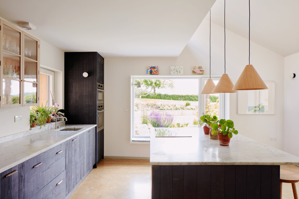 Mid-sized scandinavian single-wall eat-in kitchen in Oxfordshire with a drop-in sink, flat-panel cabinets, black cabinets, marble benchtops, panelled appliances, concrete floors, with island and grey benchtop.
