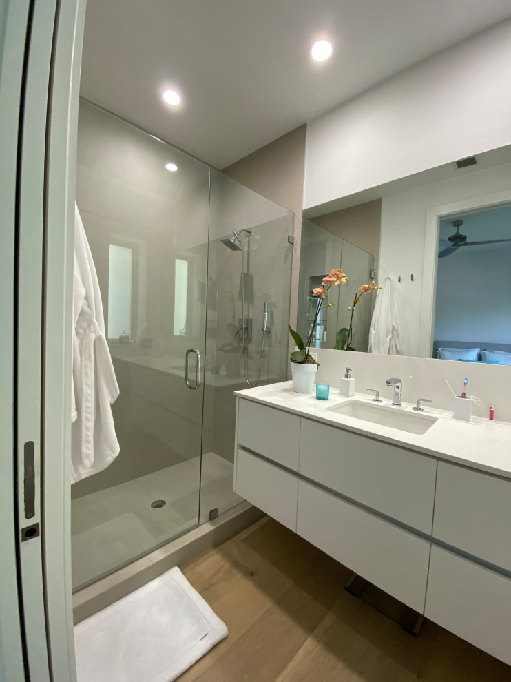 Photo of a large modern kids bathroom in Miami with flat-panel cabinets, white cabinets, a one-piece toilet, gray tile, porcelain tile, white walls, light hardwood floors, an undermount sink, quartzite benchtops, grey floor, a hinged shower door, white benchtops, a single vanity and a floating vanity.