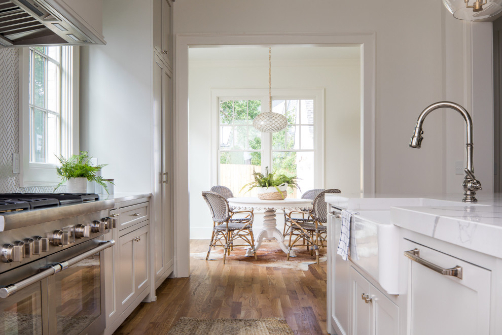 Kitchen pantry - mid-sized transitional light wood floor and brown floor kitchen pantry idea in Atlanta with a farmhouse sink, beaded inset cabinets, white cabinets, quartz countertops, white backsplash, porcelain backsplash, paneled appliances, an island and white countertops