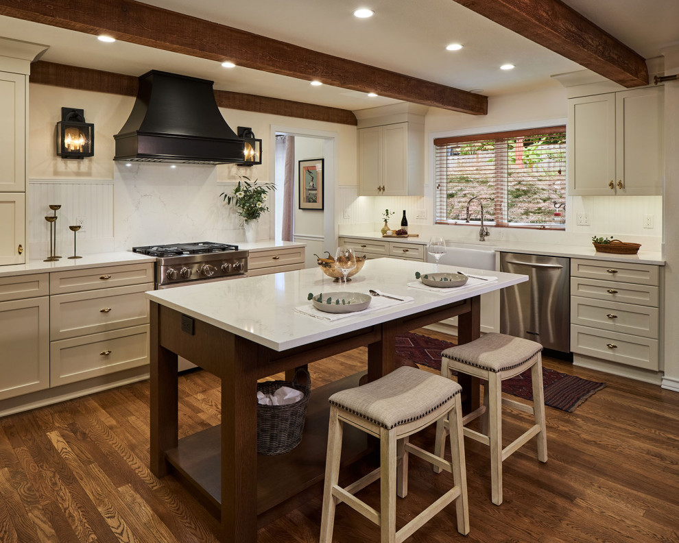 Inspiration for a large timeless u-shaped medium tone wood floor, brown floor and exposed beam enclosed kitchen remodel in Portland with a farmhouse sink, shaker cabinets, beige cabinets, quartz countertops, white backsplash, wood backsplash, stainless steel appliances, an island and white countertops