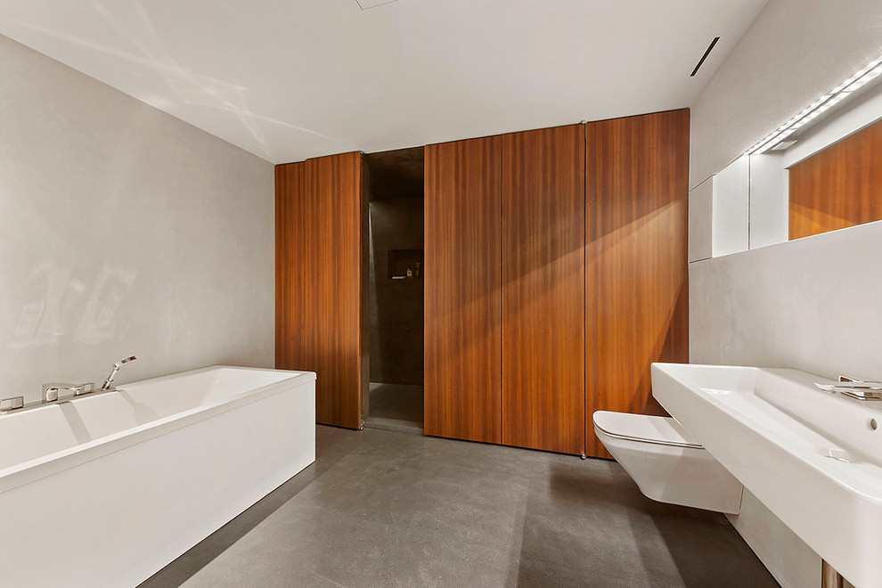 This is an example of a contemporary master bathroom in New York with a freestanding tub, a wall-mount toilet, grey walls, concrete floors and a wall-mount sink.