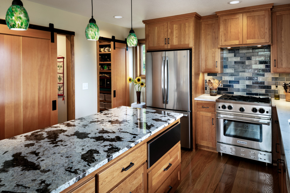 Example of a mid-sized arts and crafts u-shaped medium tone wood floor and brown floor eat-in kitchen design with an undermount sink, shaker cabinets, medium tone wood cabinets, granite countertops, blue backsplash, ceramic backsplash, stainless steel appliances, an island and multicolored countertops