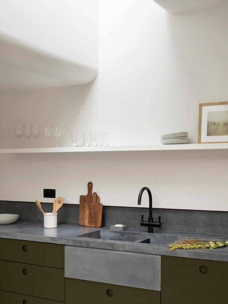 Inspiration for a mid-sized single-wall eat-in kitchen in London with a drop-in sink, flat-panel cabinets, green cabinets, concrete benchtops, grey splashback, stone slab splashback, black appliances, concrete floors, no island, grey floor and grey benchtop.