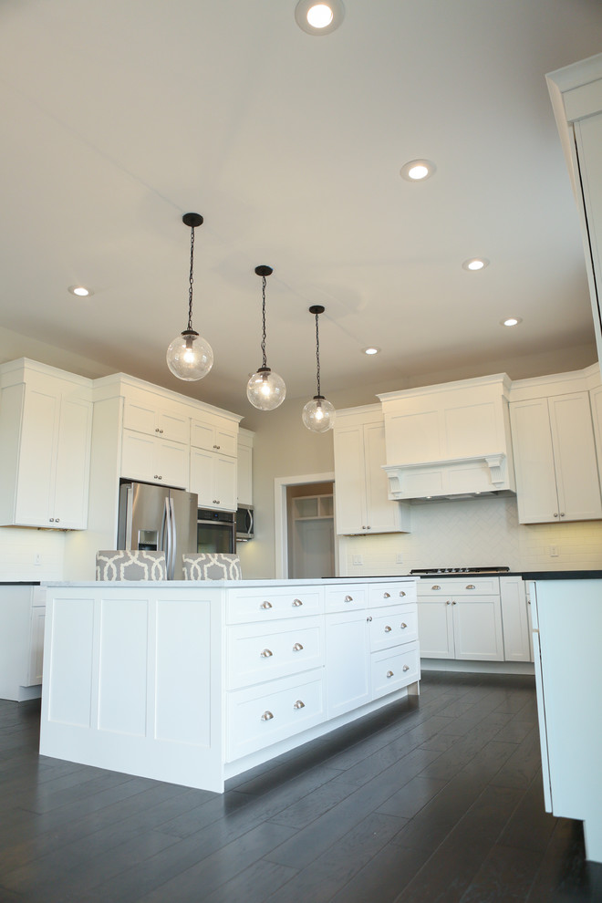 Inspiration for a large transitional u-shaped dark wood floor eat-in kitchen remodel in Chicago with a farmhouse sink, shaker cabinets, yellow cabinets, granite countertops, white backsplash, subway tile backsplash, stainless steel appliances and an island