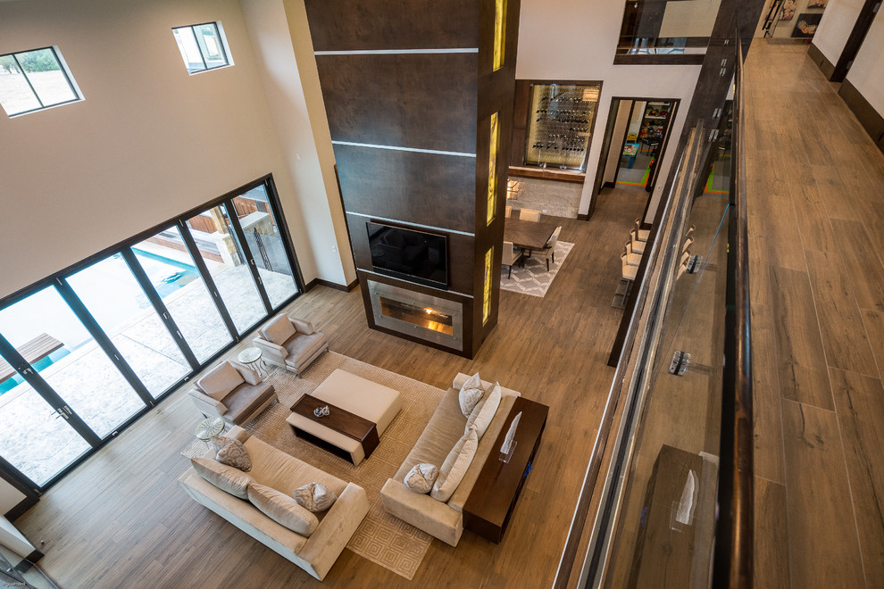 This is an example of an expansive contemporary open concept living room in Orange County with a two-sided fireplace, beige walls, porcelain floors and brown floor.