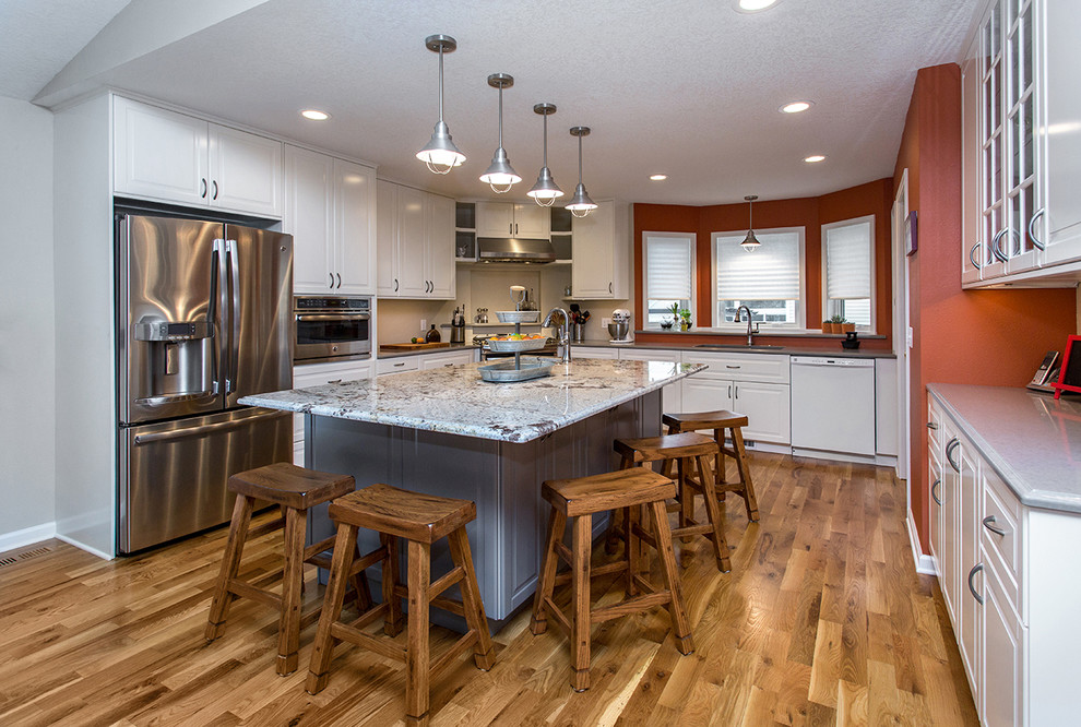 Example of a mid-sized transitional u-shaped medium tone wood floor open concept kitchen design with an undermount sink, raised-panel cabinets, white cabinets, quartz countertops, gray backsplash, porcelain backsplash, stainless steel appliances and an island