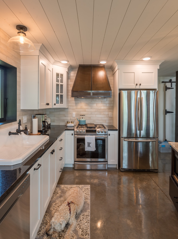 Example of a mid-sized mountain style l-shaped concrete floor and gray floor open concept kitchen design in Minneapolis with a drop-in sink, shaker cabinets, white cabinets, solid surface countertops, beige backsplash, subway tile backsplash, stainless steel appliances, an island and black countertops