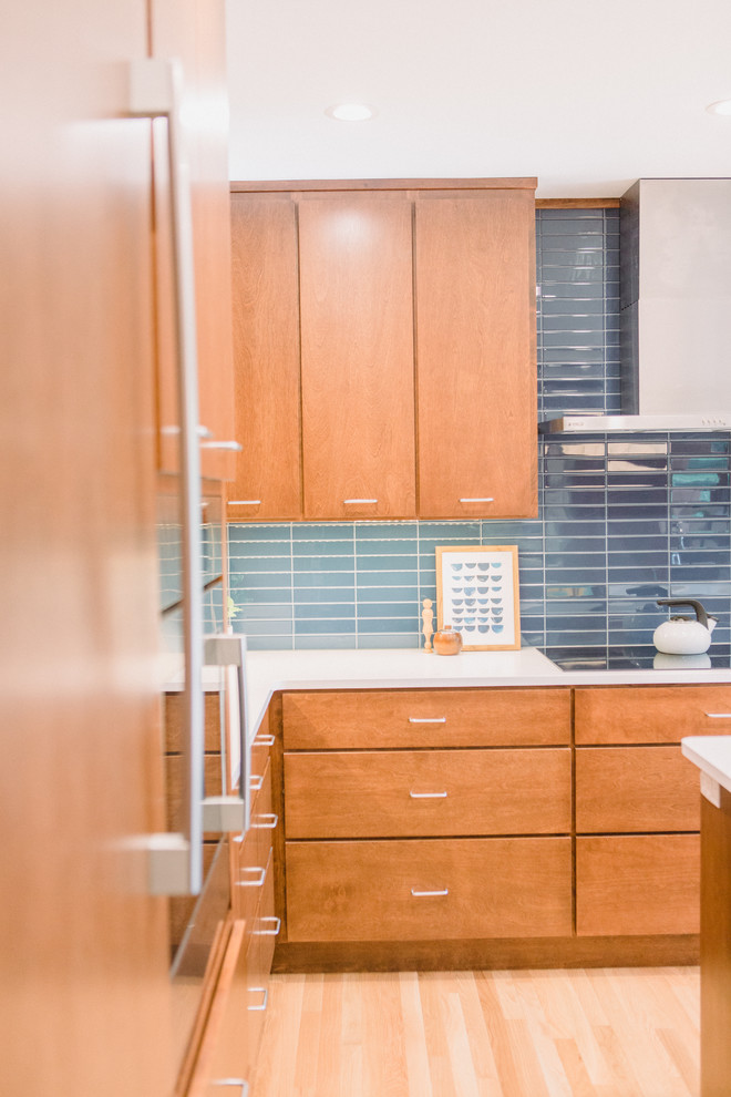 Photo of a mid-sized midcentury l-shaped open plan kitchen in Grand Rapids with an undermount sink, flat-panel cabinets, medium wood cabinets, quartz benchtops, blue splashback, ceramic splashback, panelled appliances, light hardwood floors, with island, brown floor and white benchtop.
