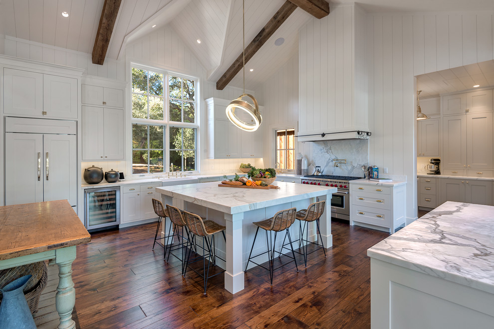 Country u-shaped kitchen in San Francisco with a farmhouse sink, shaker cabinets, white cabinets, white splashback, stone slab splashback, stainless steel appliances, dark hardwood floors, with island, brown floor and white benchtop.