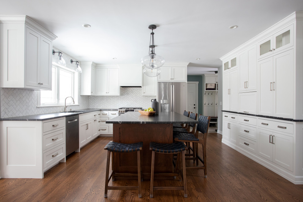 Design ideas for a large transitional u-shaped eat-in kitchen in Minneapolis with a double-bowl sink, recessed-panel cabinets, white cabinets, white splashback, stainless steel appliances, dark hardwood floors, with island and black benchtop.