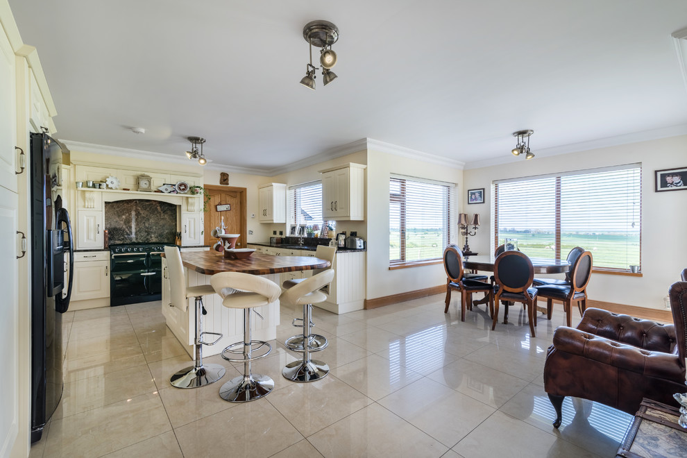 Photo of a large country l-shaped eat-in kitchen in Other with shaker cabinets, white cabinets, multi-coloured splashback, black appliances, with island, beige floor, granite benchtops, ceramic floors and brown benchtop.