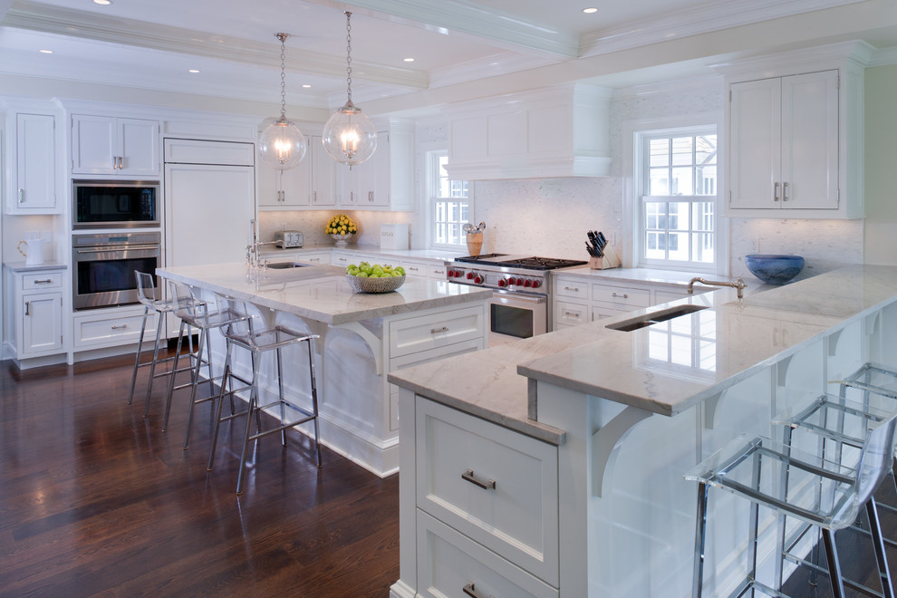 Mid-sized transitional u-shaped eat-in kitchen in Orange County with a double-bowl sink, shaker cabinets, white cabinets, marble benchtops, white splashback, stone tile splashback, white appliances, dark hardwood floors, with island and white floor.