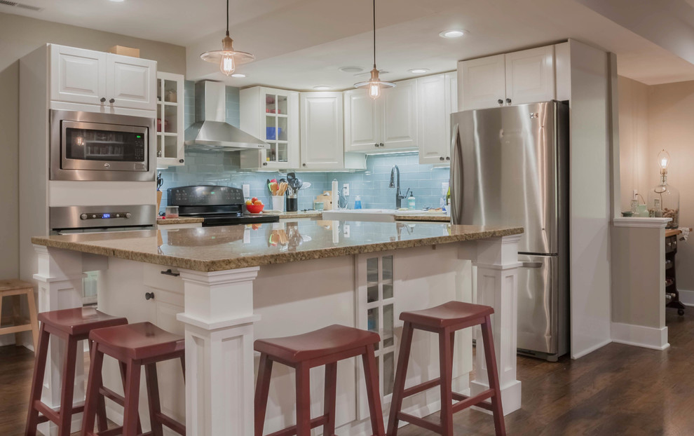 This is an example of a mid-sized traditional l-shaped eat-in kitchen in Other with a farmhouse sink, shaker cabinets, white cabinets, granite benchtops, blue splashback, glass tile splashback, stainless steel appliances, medium hardwood floors, with island, brown floor and beige benchtop.