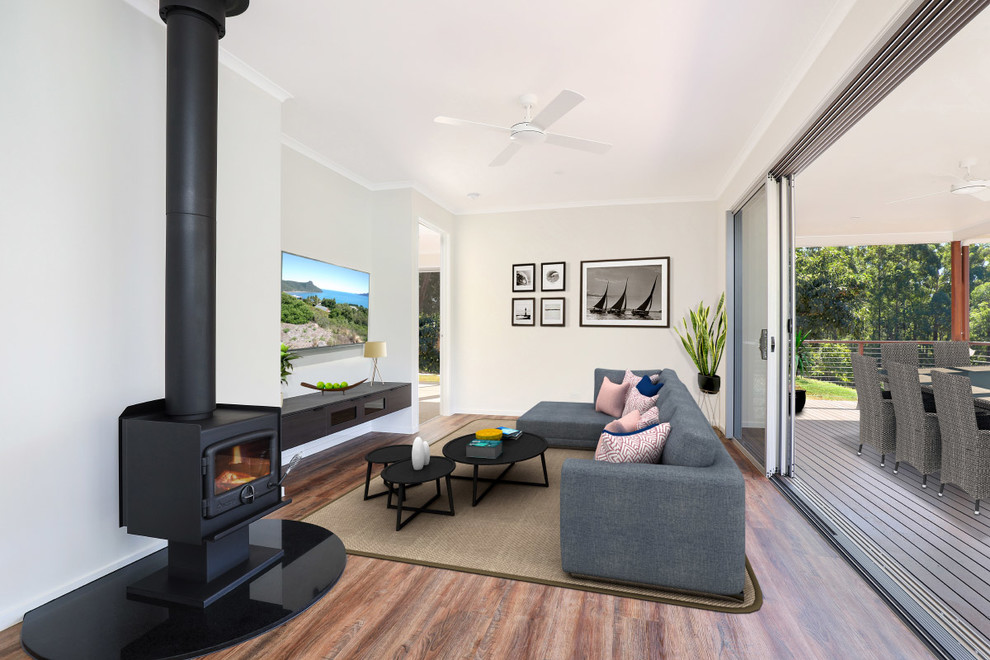 This is an example of a small modern formal open concept living room in Sunshine Coast with white walls, linoleum floors, a wood stove, a wall-mounted tv and brown floor.