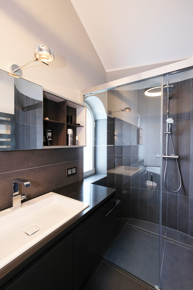 Kleines Modernes Duschbad mit flächenbündigen Schrankfronten, schwarzen Schränken, Wandtoilette mit Spülkasten, grauen Fliesen, grauer Wandfarbe, Einbauwaschbecken, grauem Boden, schwarzer Waschtischplatte, bodengleicher Dusche und Schiebetür-Duschabtrennung in Dortmund