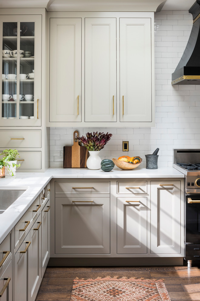 Inspiration for a large country l-shaped eat-in kitchen in New York with a double-bowl sink, shaker cabinets, beige cabinets, quartz benchtops, white splashback, ceramic splashback, black appliances, medium hardwood floors, with island, brown floor and white benchtop.