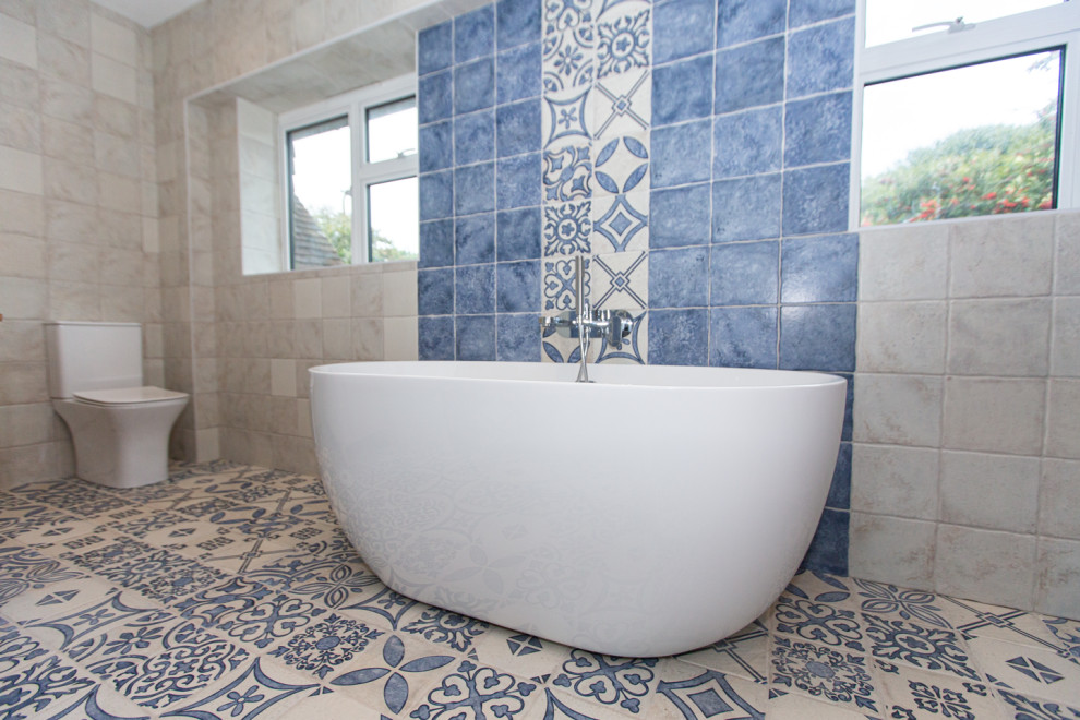 Example of a large tuscan master blue tile and ceramic tile double-sink and multicolored floor bathroom design in Sussex with medium tone wood cabinets, a freestanding vanity, a one-piece toilet, white walls, wood countertops and a hinged shower door