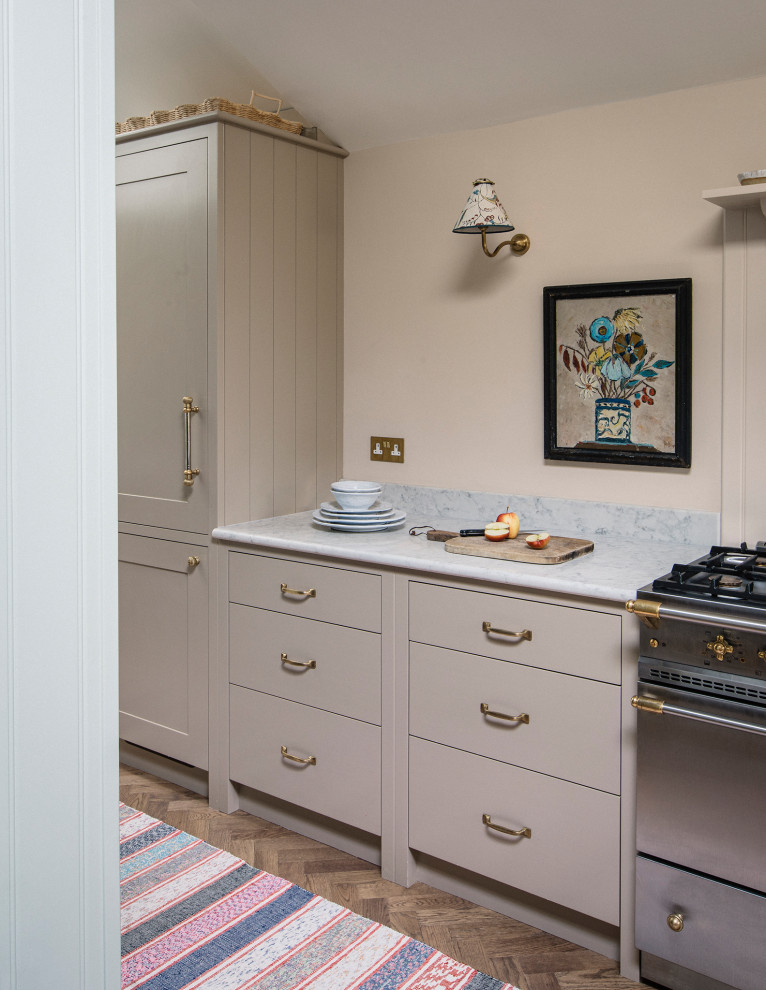 Mid-sized traditional single-wall eat-in kitchen in London with a farmhouse sink, shaker cabinets, beige cabinets, quartzite benchtops, beige splashback, black appliances, with island, brown floor and grey benchtop.