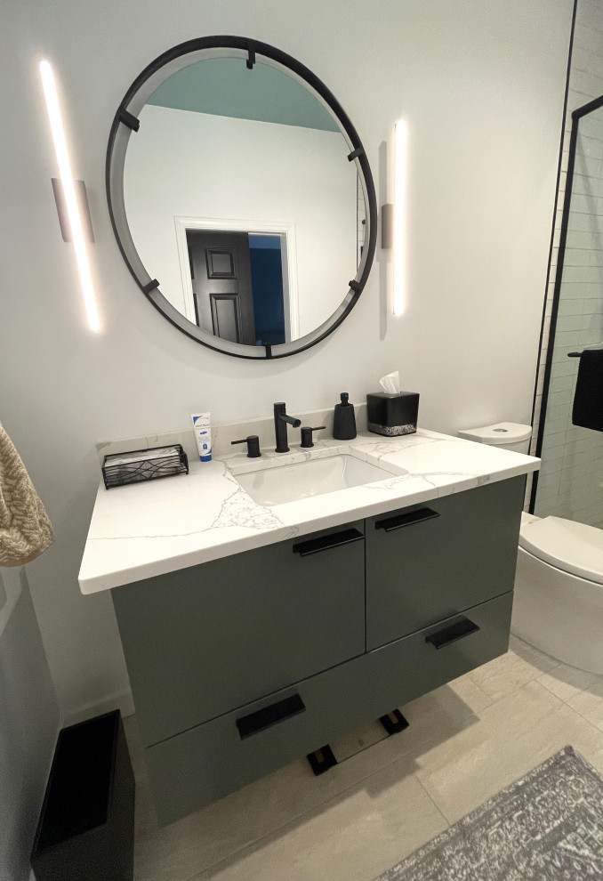На фото: маленькая главная ванная комната в стиле модернизм с плоскими фасадами, зелеными фасадами, душем без бортиков, унитазом-моноблоком, белой плиткой, керамогранитной плиткой, белыми стенами, полом из керамической плитки, врезной раковиной, столешницей из искусственного кварца, бежевым полом, душем с распашными дверями, белой столешницей, тумбой под одну раковину и подвесной тумбой для на участке и в саду