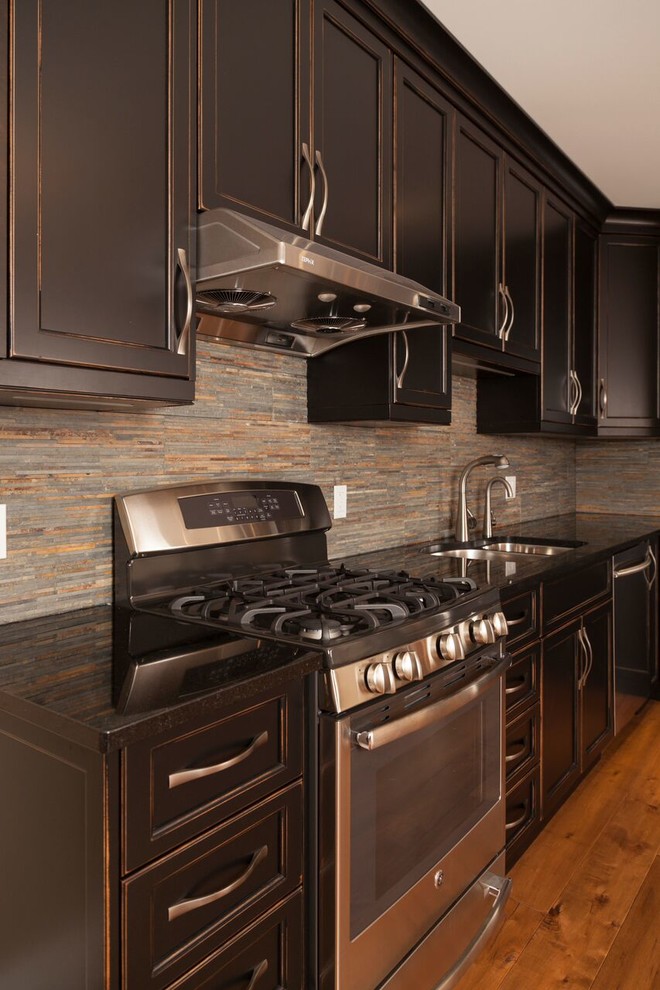 Example of a mid-sized transitional l-shaped medium tone wood floor open concept kitchen design in Toronto with a double-bowl sink, recessed-panel cabinets, dark wood cabinets, solid surface countertops, gray backsplash, stone tile backsplash, stainless steel appliances and no island