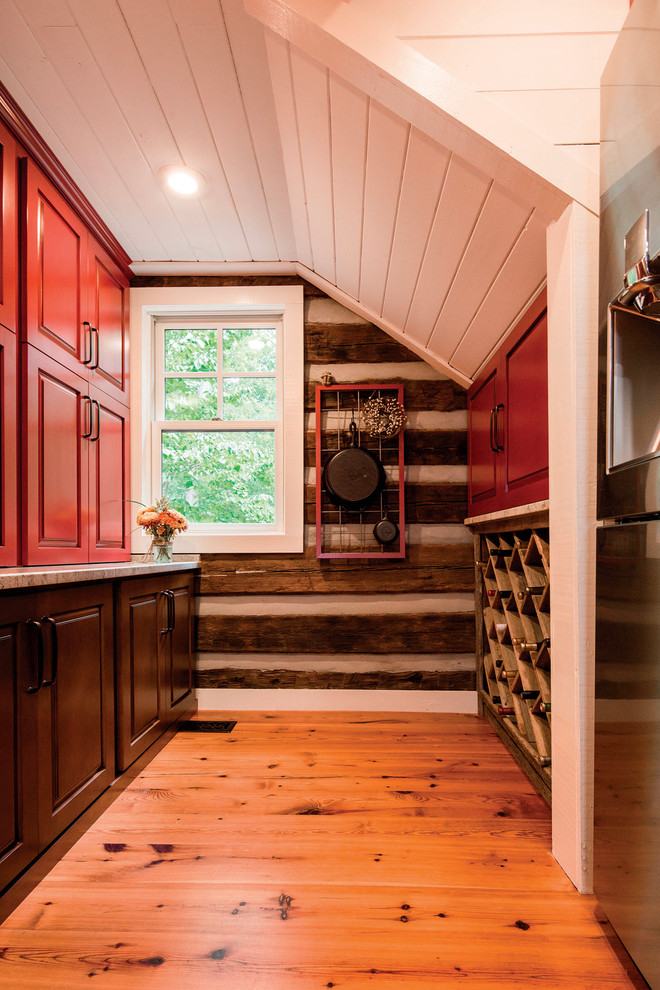 Example of a large mountain style l-shaped brown floor kitchen design with a farmhouse sink, raised-panel cabinets, brown cabinets, stainless steel appliances and an island
