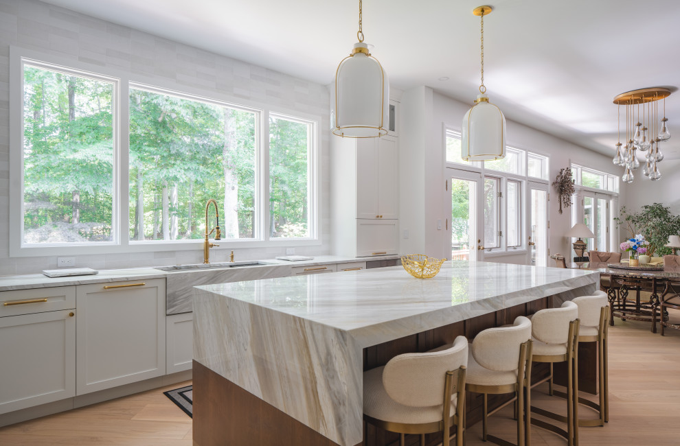 Example of a large transitional u-shaped light wood floor and brown floor eat-in kitchen design in DC Metro with a farmhouse sink, shaker cabinets, white cabinets, quartzite countertops, white backsplash, ceramic backsplash, stainless steel appliances, an island and white countertops