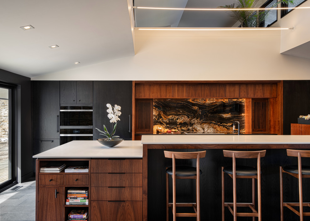 Photo of a midcentury single-wall eat-in kitchen in Kansas City with an undermount sink, flat-panel cabinets, medium wood cabinets, quartz benchtops, multi-coloured splashback, granite splashback, panelled appliances, slate floors, with island, black floor, white benchtop and vaulted.
