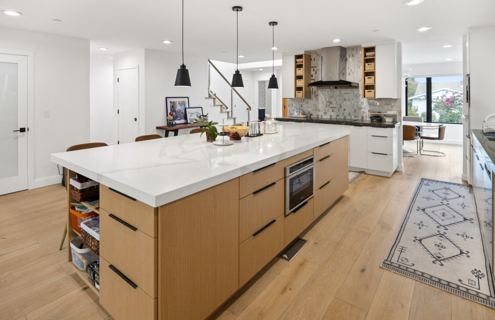 Large minimalist l-shaped light wood floor and yellow floor eat-in kitchen photo in San Francisco with a drop-in sink, flat-panel cabinets, light wood cabinets, gray backsplash, glass tile backsplash, stainless steel appliances, an island and white countertops