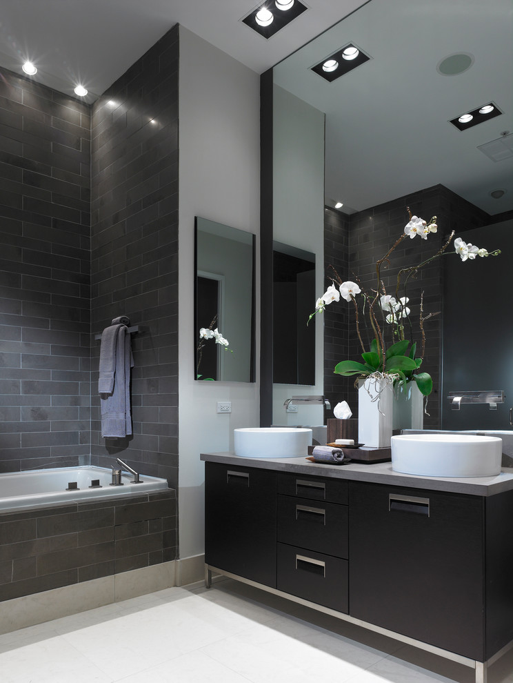 Photo of a contemporary bathroom in New York with a vessel sink, flat-panel cabinets, black cabinets, a drop-in tub, a shower/bathtub combo, gray tile, grey walls and grey benchtops.