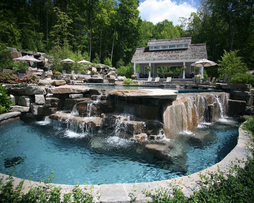This is an example of a large contemporary backyard custom-shaped infinity pool in Other with a pool house and natural stone pavers.