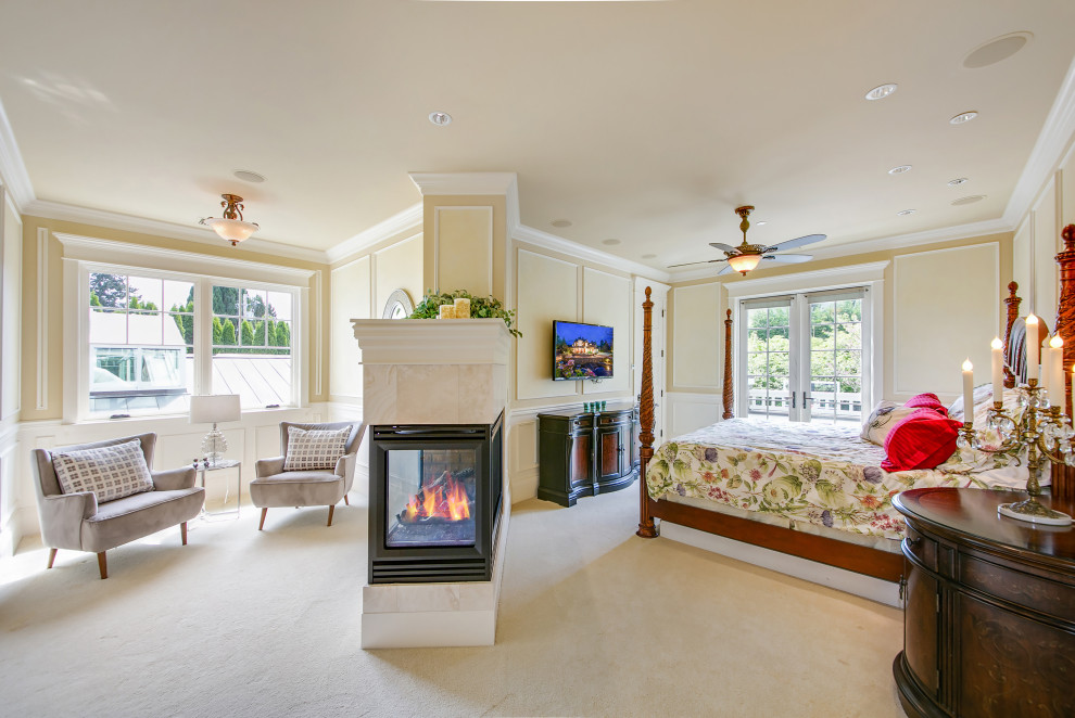 This is an example of an expansive traditional master bedroom in Seattle with beige walls, carpet, a two-sided fireplace, a metal fireplace surround and beige floor.