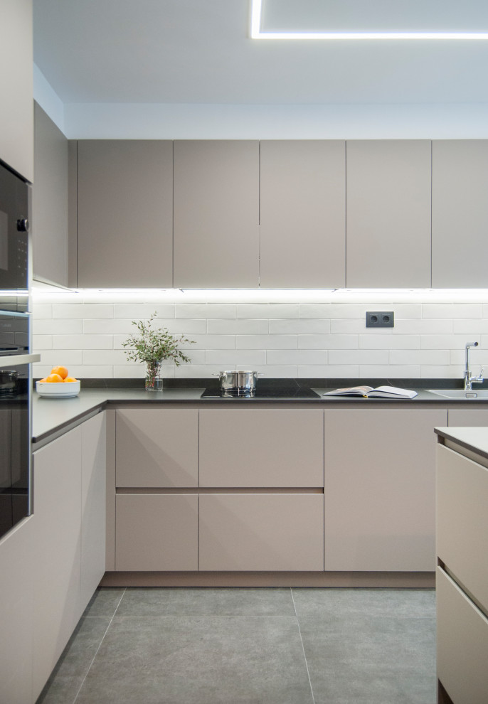 Example of a mid-sized l-shaped gray floor open concept kitchen design in Bilbao with flat-panel cabinets, gray cabinets, granite countertops, white backsplash, black appliances, an island and black countertops