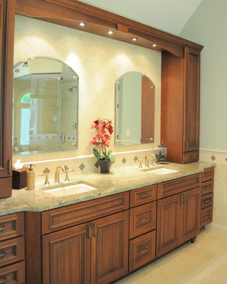 Photo of a large traditional master bathroom in Cleveland with an undermount sink, raised-panel cabinets, medium wood cabinets, granite benchtops, an undermount tub, a corner shower, a one-piece toilet, beige tile, stone tile, green walls, travertine floors, beige floor, a hinged shower door and green benchtops.