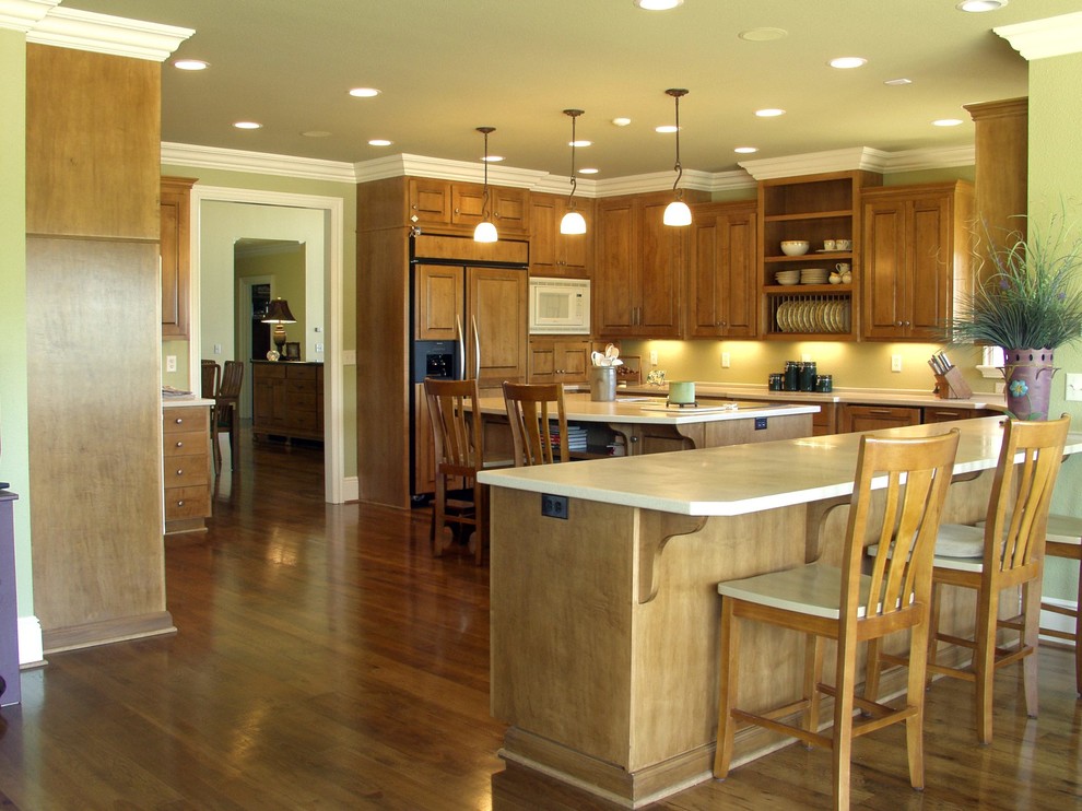 Kitchen pantry - l-shaped medium tone wood floor kitchen pantry idea with an undermount sink, raised-panel cabinets, medium tone wood cabinets, solid surface countertops, yellow backsplash, paneled appliances and two islands