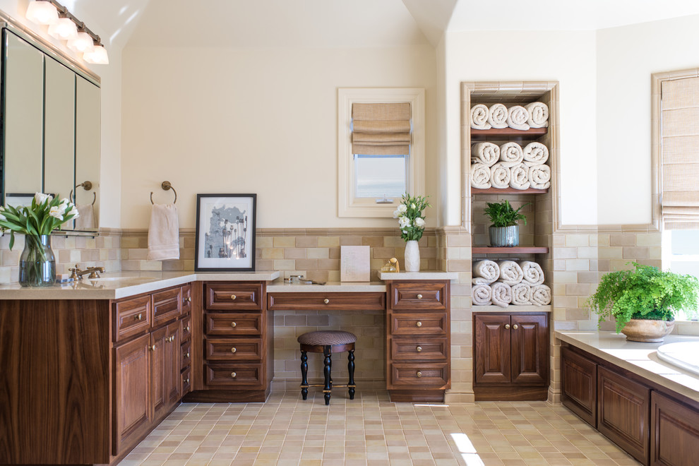 Inspiration for a large mediterranean master bathroom in Los Angeles with raised-panel cabinets, dark wood cabinets, a drop-in tub, beige walls, a one-piece toilet, beige tile, gray tile, stone tile, ceramic floors, an undermount sink, solid surface benchtops and beige floor.