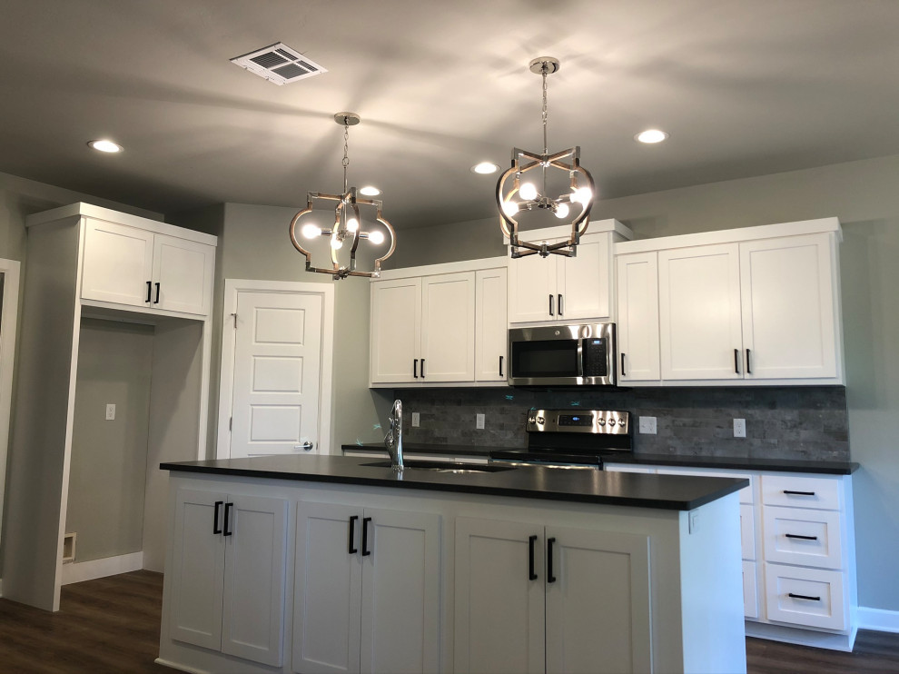 This is an example of a mid-sized transitional kitchen in Oklahoma City with a double-bowl sink, shaker cabinets, white cabinets, granite benchtops, grey splashback, ceramic splashback, stainless steel appliances, vinyl floors, with island and black benchtop.