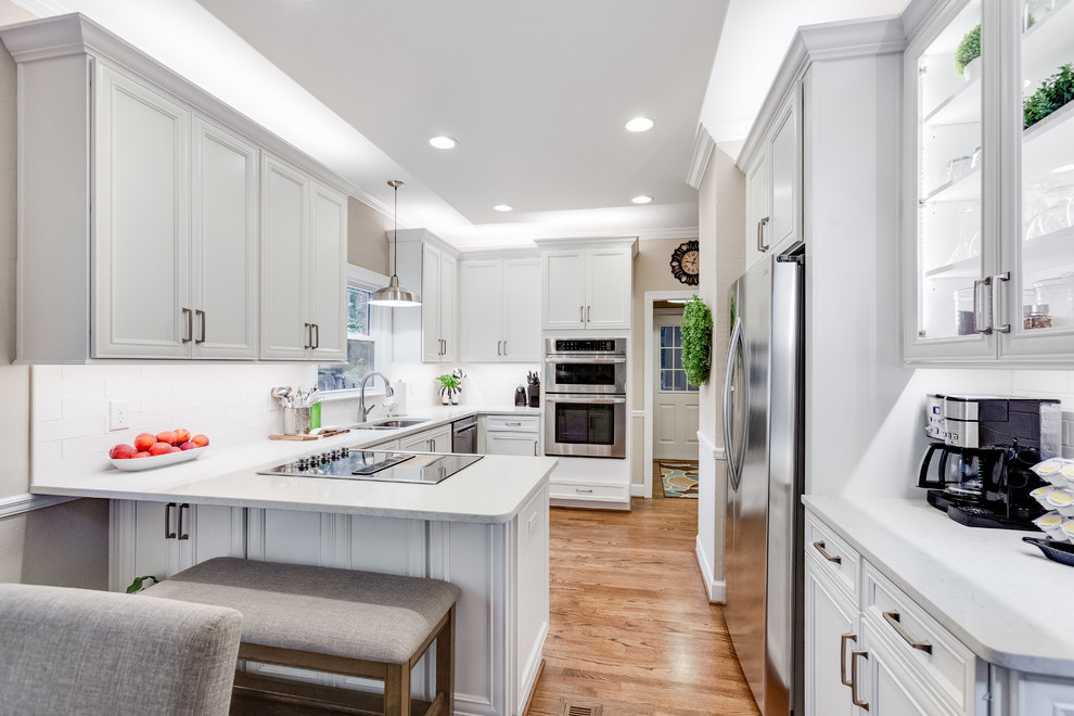 Inspiration for a mid-sized transitional u-shaped medium tone wood floor and brown floor eat-in kitchen remodel in Birmingham with a double-bowl sink, recessed-panel cabinets, white cabinets, quartz countertops, white backsplash, subway tile backsplash, stainless steel appliances, a peninsula and white countertops