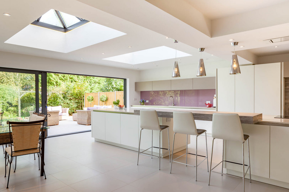 Photo of a contemporary galley eat-in kitchen in Oxfordshire with flat-panel cabinets, white cabinets, glass sheet splashback, with island, grey floor and white benchtop.