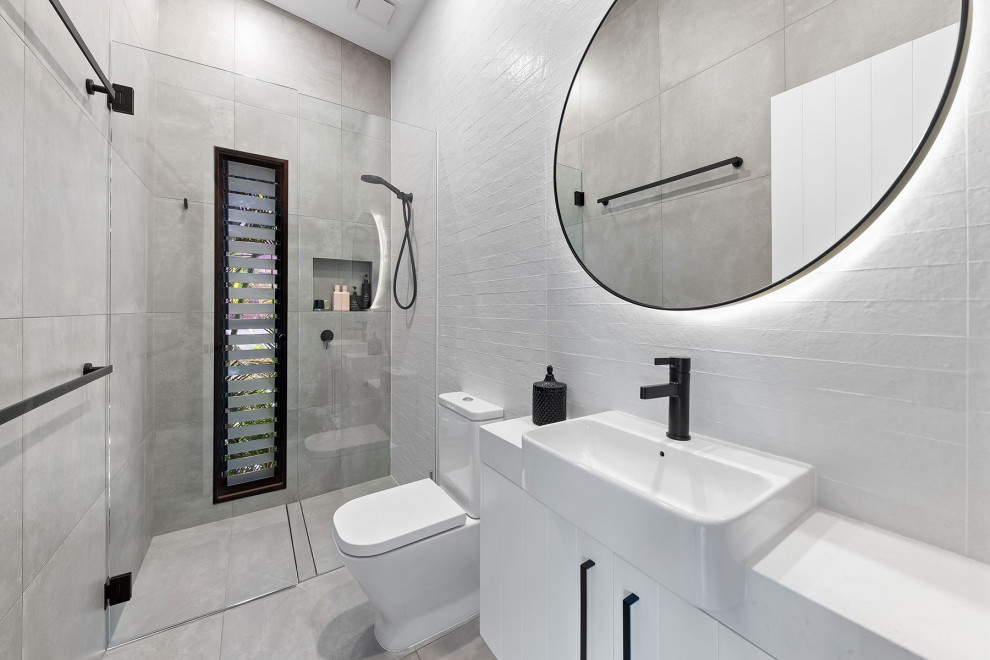 Exempel på ett litet maritimt vit vitt badrum, med möbel-liknande, vita skåp, en öppen dusch, en toalettstol med hel cisternkåpa, grå kakel, porslinskakel, vita väggar, klinkergolv i porslin, ett fristående handfat, bänkskiva i kvarts, grått golv och dusch med gångjärnsdörr