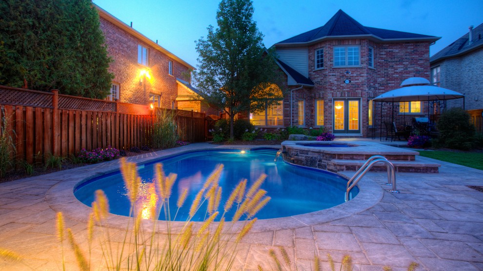 This is an example of a mid-sized traditional backyard custom-shaped natural pool in Toronto with a pool house and natural stone pavers.
