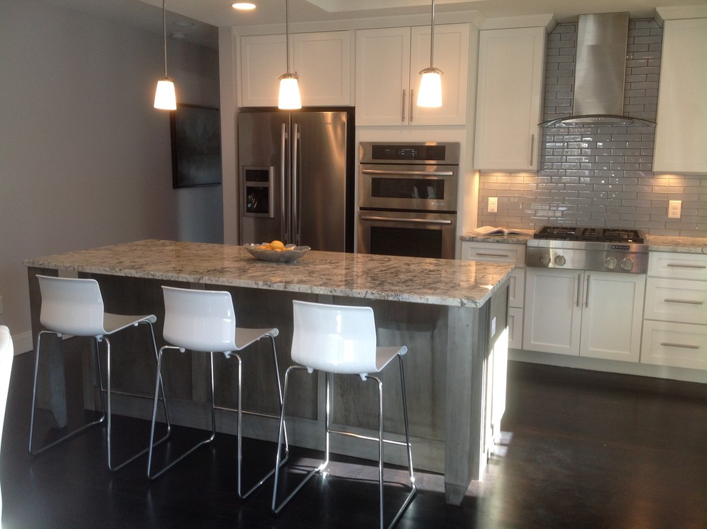 Example of a mid-sized transitional galley dark wood floor eat-in kitchen design in Denver with a double-bowl sink, recessed-panel cabinets, white cabinets, granite countertops, gray backsplash, ceramic backsplash, stainless steel appliances and an island