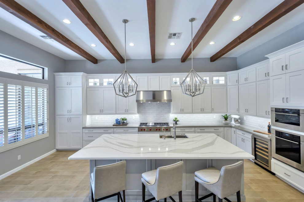 Large transitional u-shaped porcelain tile, beige floor and exposed beam enclosed kitchen photo in Phoenix with a farmhouse sink, shaker cabinets, white cabinets, quartz countertops, white backsplash, glass tile backsplash, stainless steel appliances, an island and white countertops