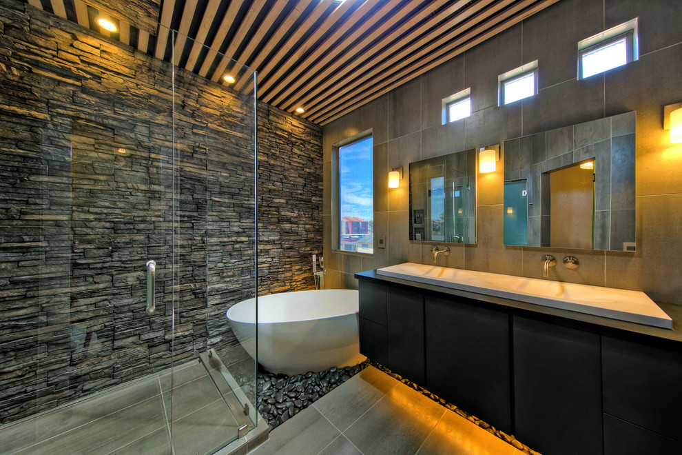 This is an example of a mid-sized contemporary master bathroom in Phoenix with flat-panel cabinets, dark wood cabinets, a freestanding tub, a corner shower, a one-piece toilet, gray tile, porcelain tile, grey walls, porcelain floors, a wall-mount sink and solid surface benchtops.