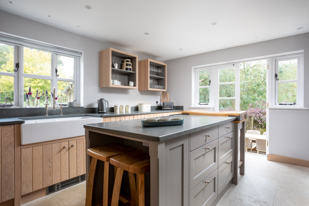 Mid-sized beach style galley separate kitchen in Gloucestershire with a farmhouse sink, shaker cabinets, medium wood cabinets, with island, beige floor, grey benchtop, grey splashback and porcelain floors.