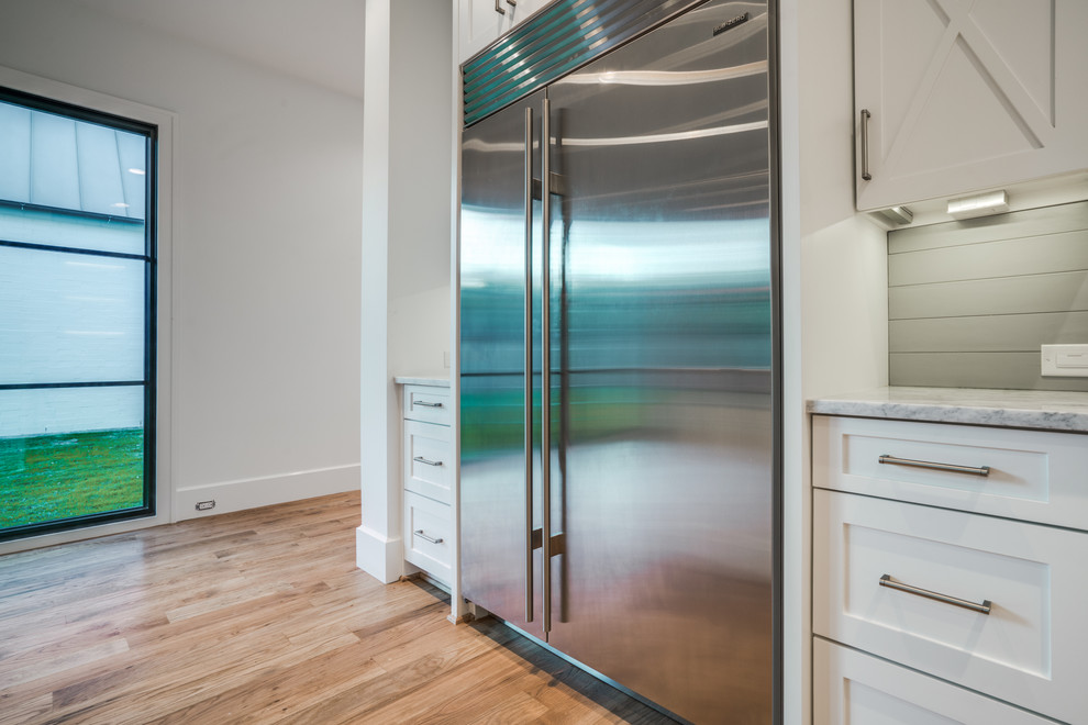 Kitchen - large transitional single-wall light wood floor kitchen idea in Dallas with a double-bowl sink, shaker cabinets, white cabinets, marble countertops, white backsplash, stainless steel appliances and an island
