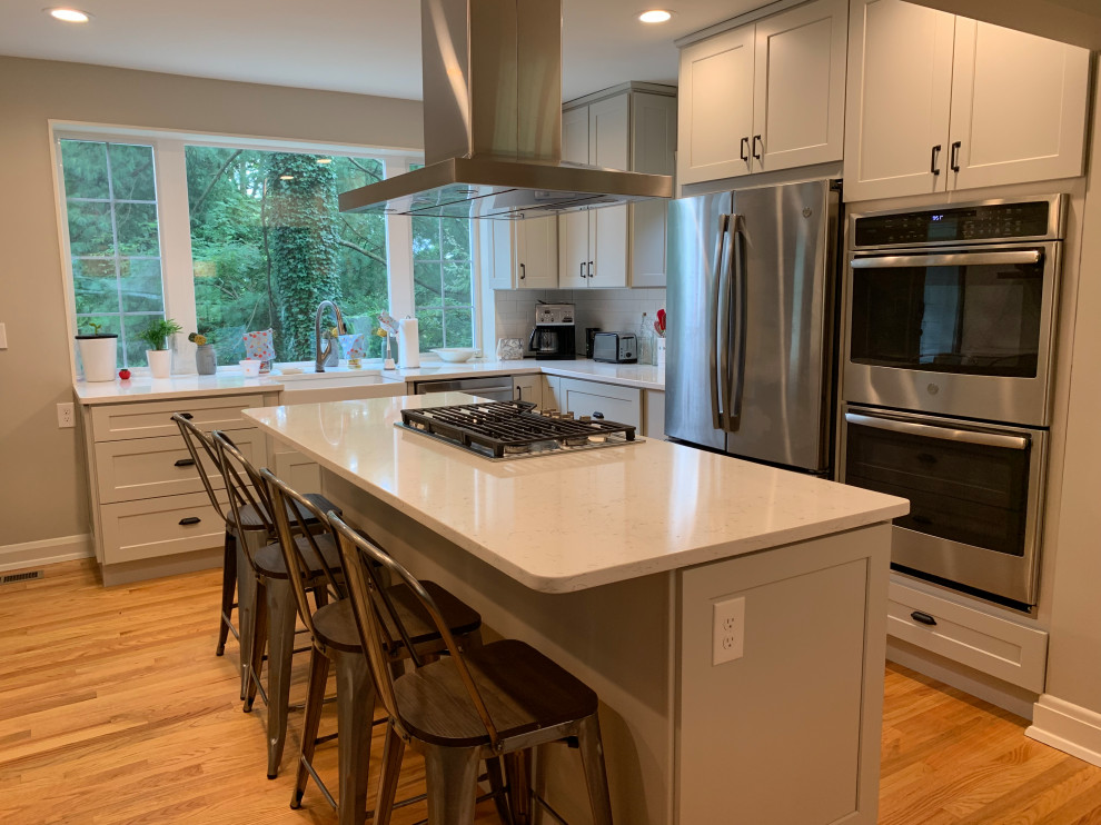Inspiration for a mid-sized transitional l-shaped medium tone wood floor eat-in kitchen remodel in Baltimore with a farmhouse sink, shaker cabinets, gray cabinets, quartz countertops, white backsplash, subway tile backsplash, stainless steel appliances, an island and white countertops
