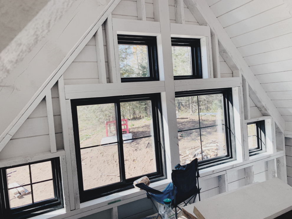 Imagen de dormitorio machihembrado, tipo loft y abovedado de estilo de casa de campo pequeño con paredes blancas, suelo de madera clara, estufa de leña, suelo beige y machihembrado